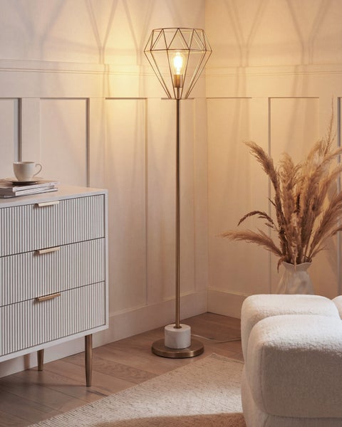 Goldene Stehleuchte mit Diamant-Drahtschirm und Marmorfuß in hellem, organisiertem Wohnraum mit weißer Kommode und Pampasgras.