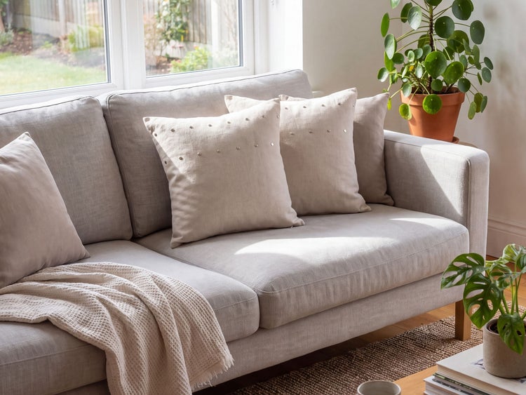 Helles Sofa mit Dekokissen, Überwurf und Zimmerpflanzen in einem sonnendurchfluteten Wohnzimmer.