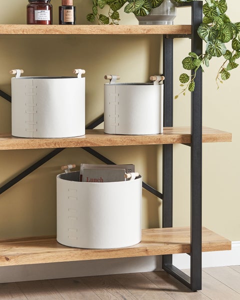 Drei runde weiße Aufbewahrungskörbe mit Holzgriffen in einem modernen Standregal aus Holz und schwarzem Metall für ein organisiertes Zuhause.