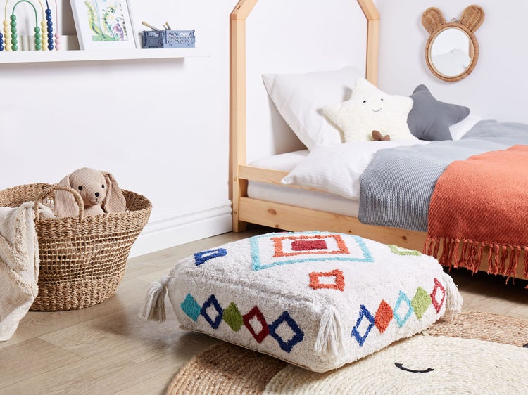 Kinderzimmer mit Holzbett, Korb, Spielzeug und weißem Pouf mit bunten geometrischen Mustern