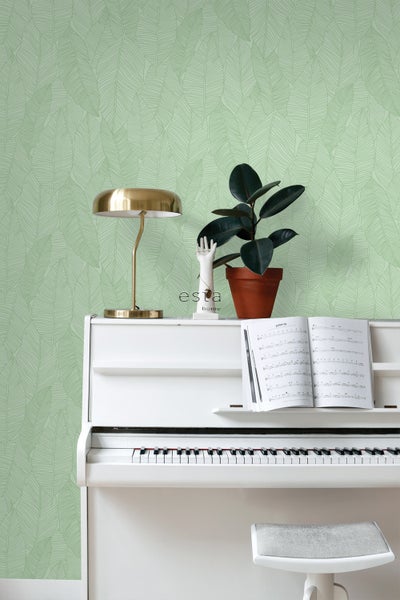 Dekorative Tapete mit Blattmuster hinter einem weißen Klavier mit Notenblatt, einer Lampe und einer Zimmerpflanze.