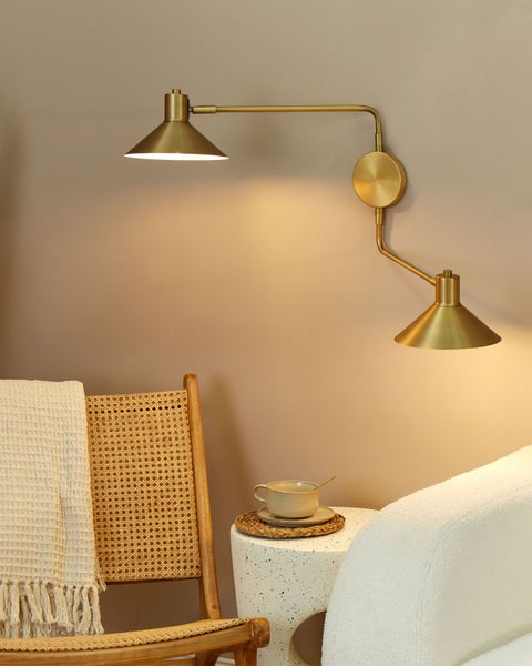 Zweiflammige Wandleuchte aus Messing in einer gemütlichen Leseecke mit Rattanstuhl und Beistelltisch.