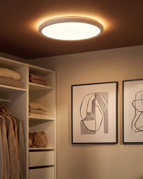Runde LED Deckenleuchte montiert an einer Decke in einem Ankleidezimmer mit Kleiderschrank und Wandbildern.