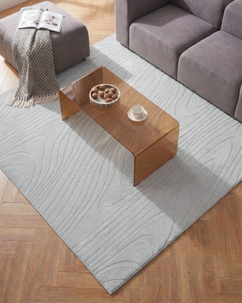 Modernes Wohnzimmer mit strukturiertem Teppich, Glastisch, Sofa und Hocker auf Holzparkett.