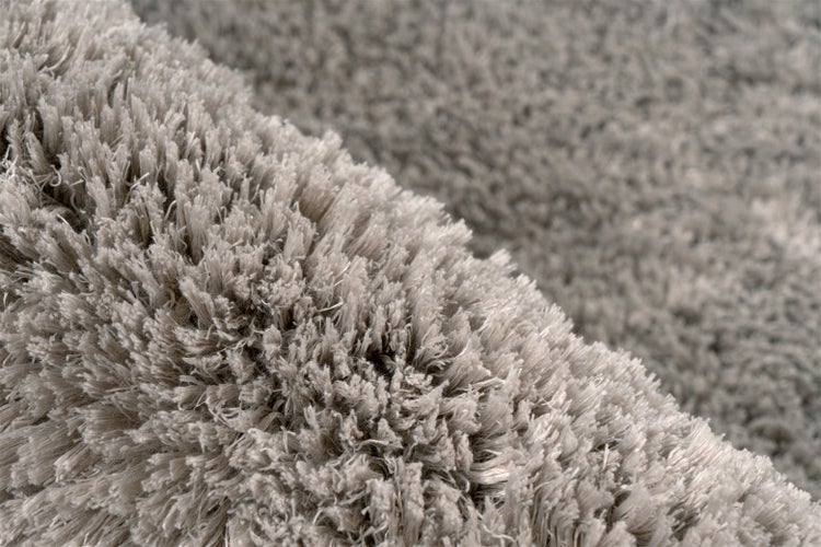 Nahaufnahme eines grauen Hochflor-Teppichs mit weicher, zotteliger Struktur.