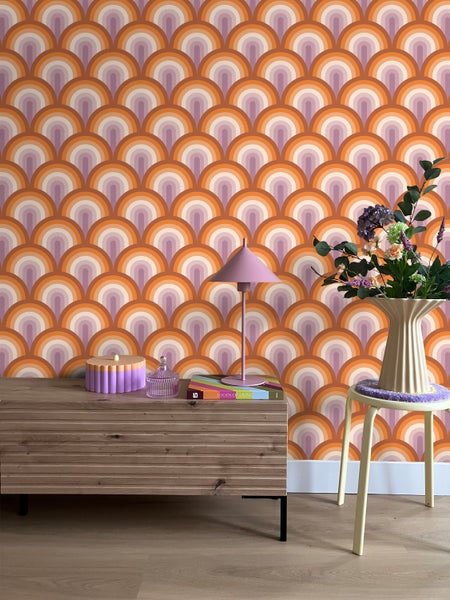 Raumansicht mit Tapete im Retro-Design, Holzkommode, Tischlampe und Blumenarrangement