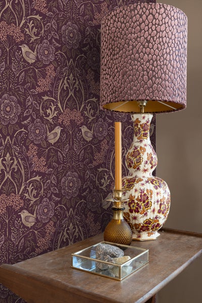 Dekoratives Stillleben mit gemusterter Tapete, Tischlampe und Kerze