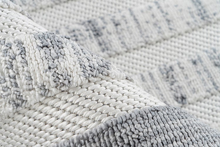 Nahaufnahme eines grau-weißen Teppichs mit gewebtem Zickzack-Muster und weicher Textur.