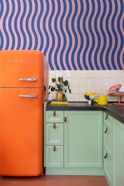 Küchenszene mit einem orangefarbenen SMEG Kühlschrank und mintgrünen Küchenschränken unter einer schwarzen Arbeitsplatte