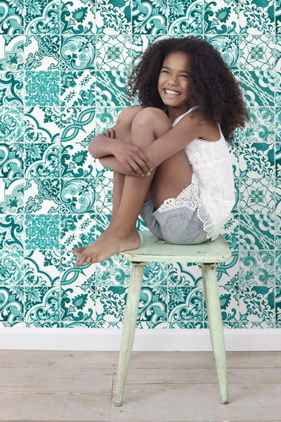 Mädchen sitzt auf einem Hocker vor einer Wand mit floralen Fliesen