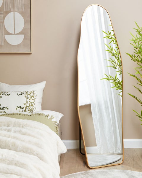 Schlafzimmerszene mit einem Spiegel mit unregelmäßigem Rahmen, Bett und Deko-Elementen.