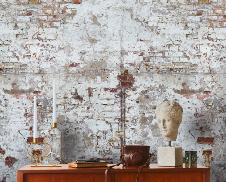 Dekorative Szene mit einer Büste, Kerzenständer und Vintage-Kamera auf einem Holzschrank vor einer Backsteinmauer.