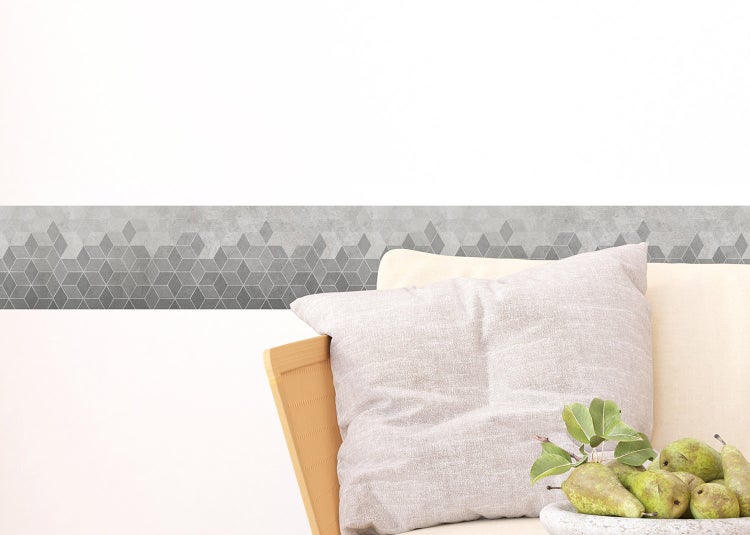 Tapetenbordüre mit geometrischem Muster in einem hellen Wohnzimmer mit modernem Sessel, Beistelltisch und buntem Teppich.