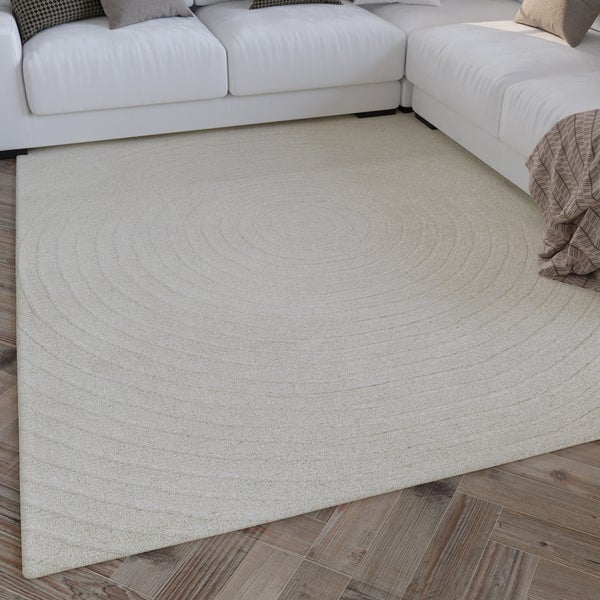 Heller, moderner Wohnbereich mit beigefarbenem, strukturiertem Teppich mit konzentrischen Kreisen vor einem weißen Sofa auf Holzparkett.