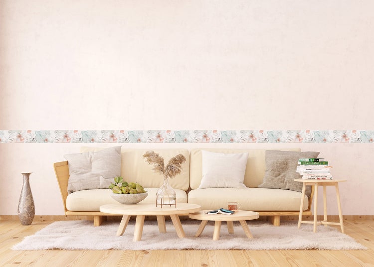 Wandbordüre mit Blumenmuster in einem hellen Wohnzimmer mit Sofa, Holztischen und Teppich.
