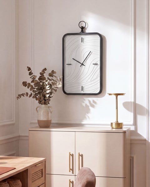 Moderne rechteckige Wanduhr mit Wellenmuster auf dem Zifferblatt, montiert an einer hellen Wand über einem Sideboard.