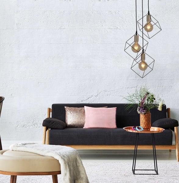 Wohnzimmer mit Sofa, Kissen, Beistelltisch, Hocker und geometrischen Pendelleuchten