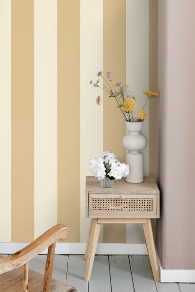 Vliestapete mit breiten vertikalen Streifen hinter einem Nachttisch aus Holz mit Wiener Geflecht und Vasen mit Blumen.