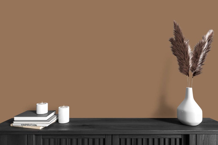 Modern eingerichteter Raum mit brauner Wandfarbe, schwarzem Sideboard aus Holz, weißen Kerzen und einer Vase mit Pampasgras.