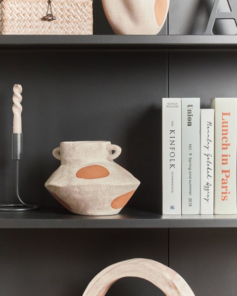 Dekorative Gegenstände auf einem Regal, darunter eine Kerze, eine Vase und Bücher