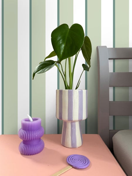 Dekorative Szene mit Zimmerpflanze in gestreiftem Topf, lila Kerze und Untersetzer auf einem Tisch