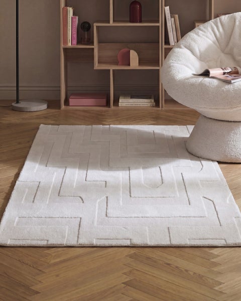 Moderner rechteckiger Teppich mit geometrischem Reliefmuster auf einem Parkettboden in einem eingerichteten Wohnbereich.