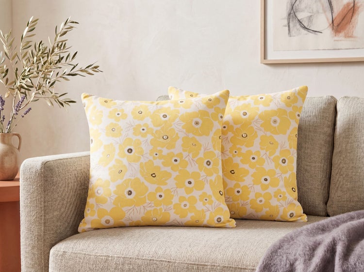 Zwei Dekokissen mit gelbem Blumenmuster auf einem hellgrauen Sofa in einem hellen Wohnzimmer.