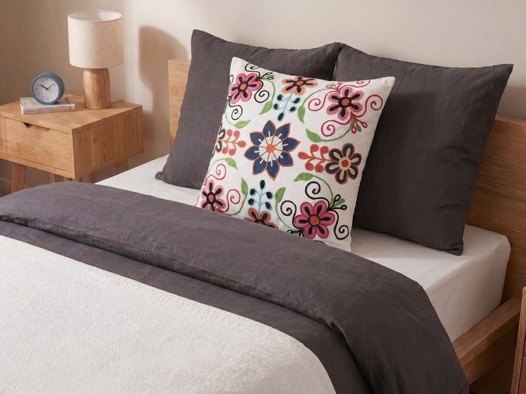 Modernes Schlafzimmer mit einem Holzbett, dunkelgrauer Bettwäsche und einem dekorativen Kissen mit bunten Blumenstickereien.