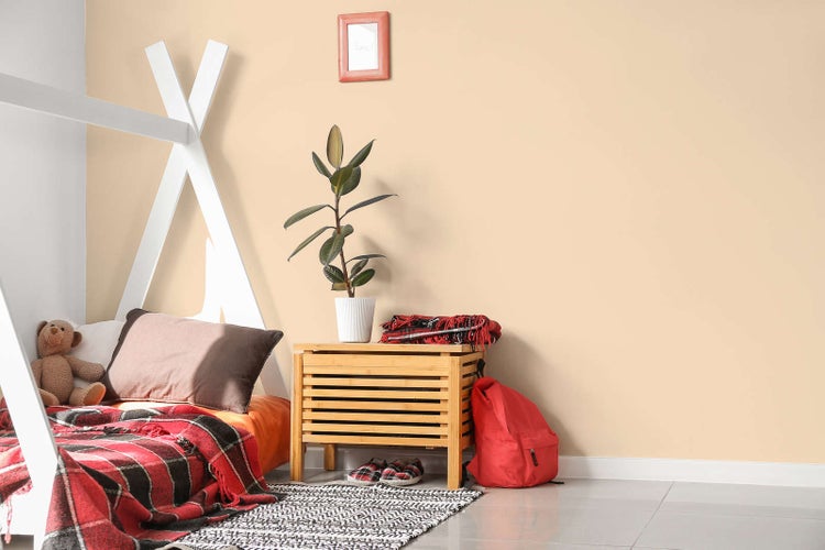 Hell gestaltetes Kinderzimmer mit pfirsichfarbener Wandfarbe, weißem Tipi-Bett, einer Holzkommode und rot-schwarz karierter Decke.