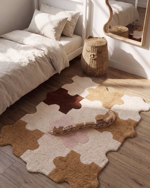 Kinderspielzimmer mit einem gemusterten Teppich in Puzzleform, einem Holzzugspielzeug, einem geflochtenen Aufbewahrungskorb und einem Holzbett.
