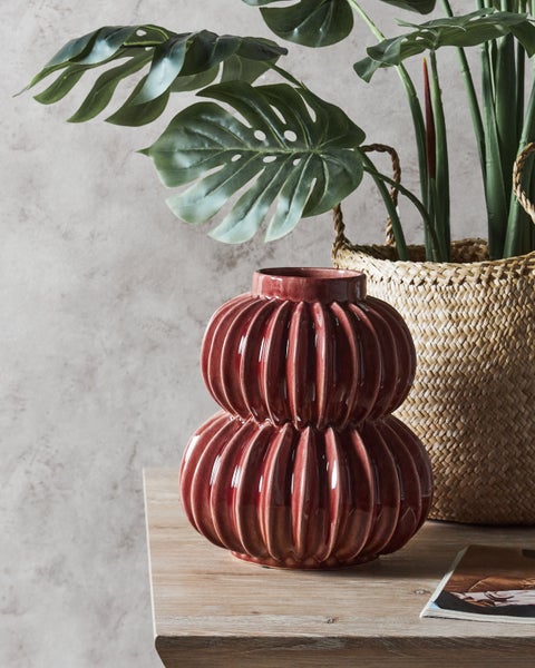 Dekorative Keramikvase auf einem Holztisch mit Zimmerpflanzen im Hintergrund