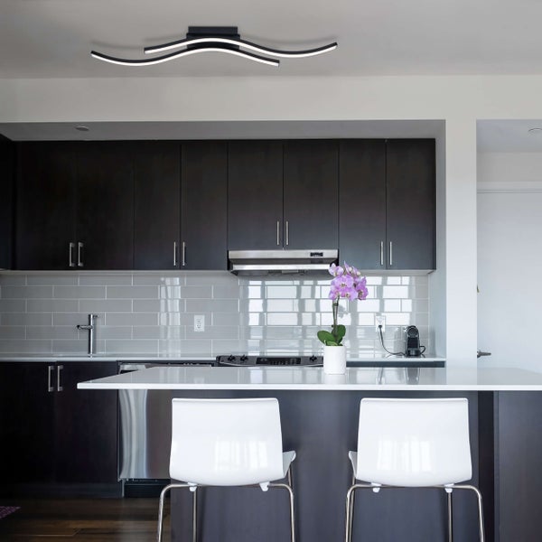 Moderne Küche mit geschwungenen LED Deckenleuchten, dunklen Schränken und Kochinsel.