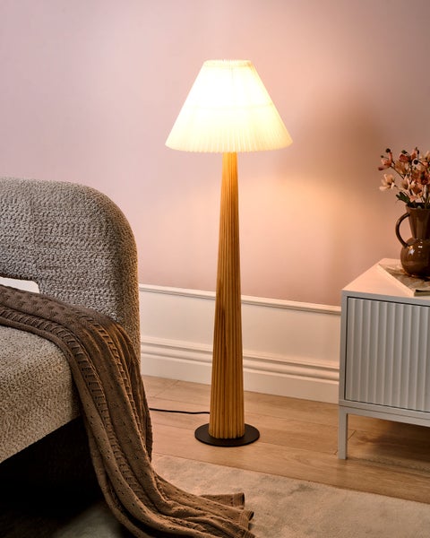 Stehleuchte mit plissiertem Schirm, Holzfuß, Sessel und Kommode in einem Wohnzimmer.