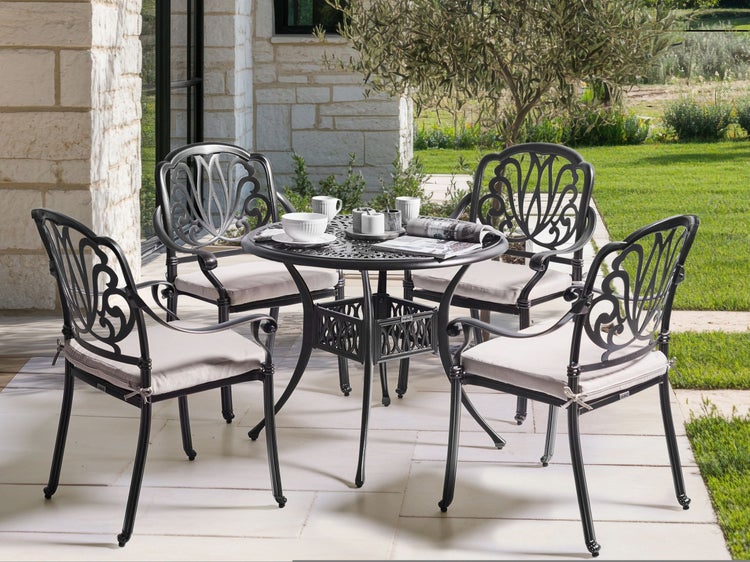 Gartenszene mit einem runden Tisch und vier Stühlen aus Metall mit Sitzkissen auf einer Terrasse