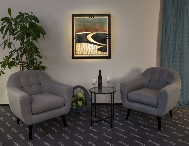 Wohnzimmer-Szene mit zwei Sesseln, einem Beistelltisch mit Wein und Gläsern und einem beleuchteten Wandbild.