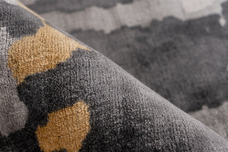 Nahaufnahme eines Teppichs mit weichem Flor und einem Muster aus grauen und goldfarbenen, fleckigen Formen.