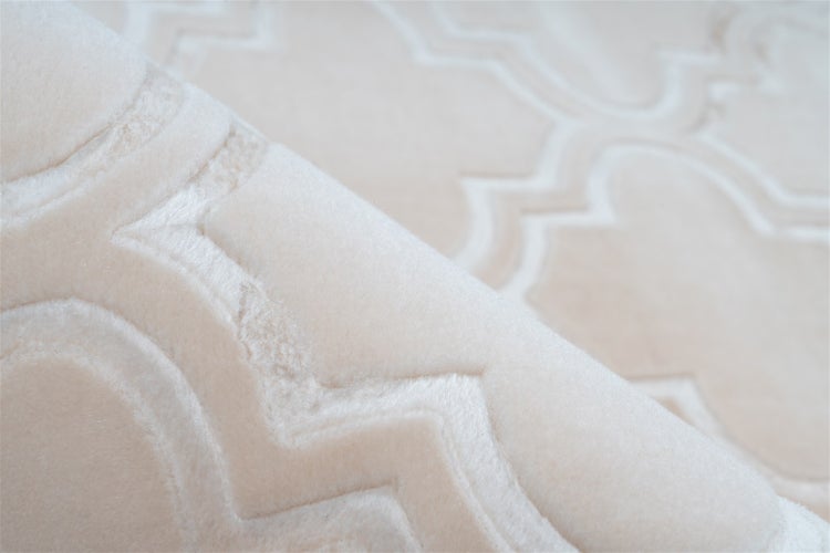 Modernes Schlafzimmer mit gemustertem Teppich in Beige, Bett mit grauen und rosa Textilien, Wand in Betonoptik und Holzmöbeln.