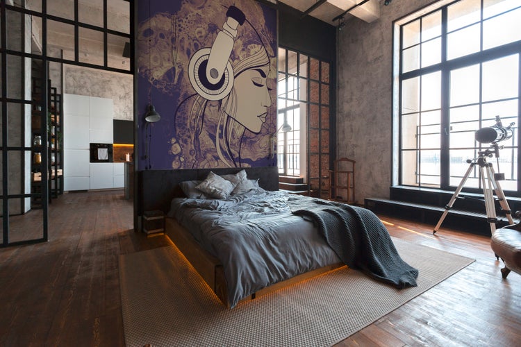Helles, geräumiges Schlafzimmer im Industrie-Stil mit großer Wandtapete, Sichtbetonwänden, dunklem Holzboden und großen Fenstern.
