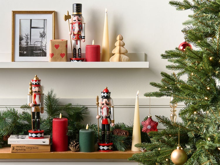 Weihnachtliche Dekoration mit Nussknackern, Kerzen und Tannengrün auf einem Regal.