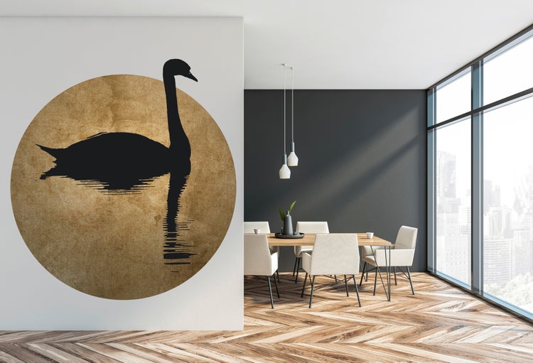 Moderne Wanddekoration mit schwarzer Schwanen-Silhouette in einem goldenen Kreis, angebracht in einem hellen Esszimmer mit Holzboden.