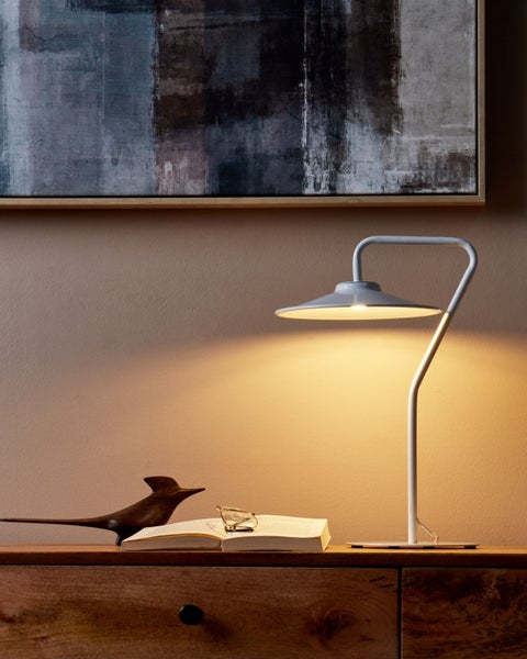 Szene mit Tischleuchte, abstrakter Wandkunst und dekorativer Holzfigur auf einem Nachttisch.