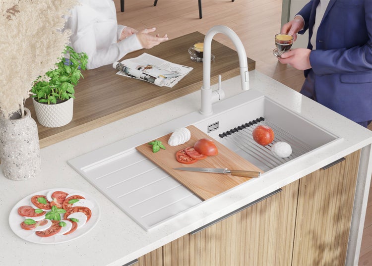 Küchenszene mit Spüle, Armatur, Schneidebrett, Tomaten und Mozzarella auf einer Arbeitsplatte.