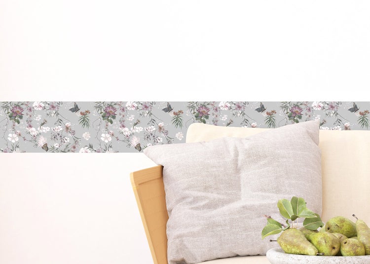 Tapetenbordüre mit Blumen- und Schmetterlingsmuster an der Wand in einem hellen Wohnzimmer.