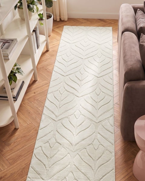 Teppich-Läufer mit Blattmuster in Relief-Optik auf Parkettboden in hellem Wohnzimmer neben Sofa und Regal.