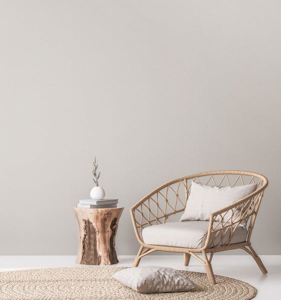 Dekoratives Interieur mit Beistelltisch aus Baumstamm, Vase mit Zweig, Bücherstapel und Rattan-Sessel.