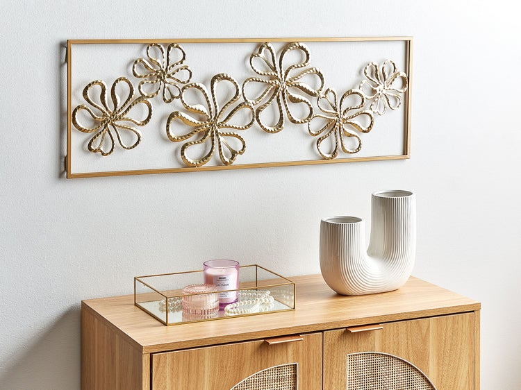 Dekoratives Arrangement mit einem Schrank, einer Blumendekoration an der Wand, einer Glasablage, einer Duftkerze und einer weißen Vase.