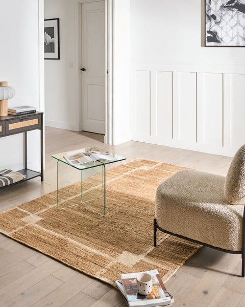 Moderner Wohnraum mit einem rechteckigen Jute-Teppich mit Gittermuster, einem Glastisch und einem beigen Sessel vor einer weißen Wand.