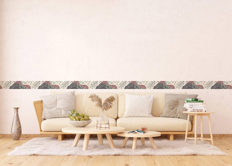 Tapetenborte mit abstrakten Formen und Blattmotiven in einem hellen Wohnzimmer über einer Couch.