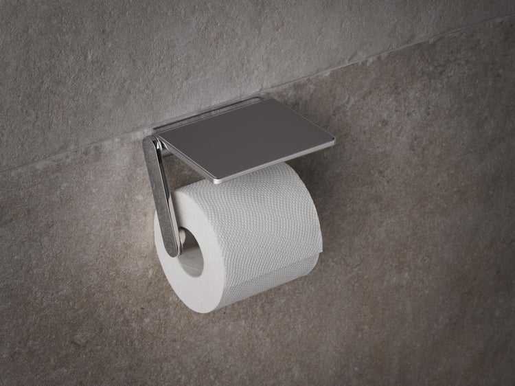 Wandmontierter Toilettenpapierhalter mit Deckel aus glänzendem Metall montiert an einer Fliesenwand mit Toilettenpapierrolle.