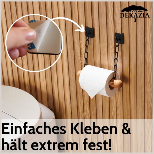 Dekazia Logo. Toilettenpapierhalter mit schwarzer Metallkette und Holzstab, selbstklebend montiert an einer Holzpaneelwand im Badezimmer.
